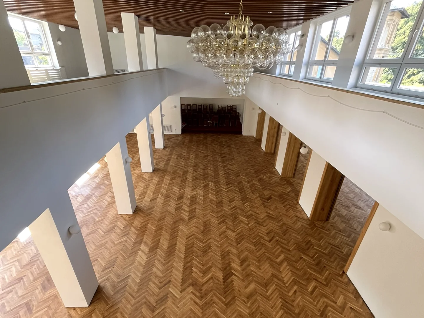 Parketová podlaha se vzorem rybí kosti v prostorném sále, pohled z galerie