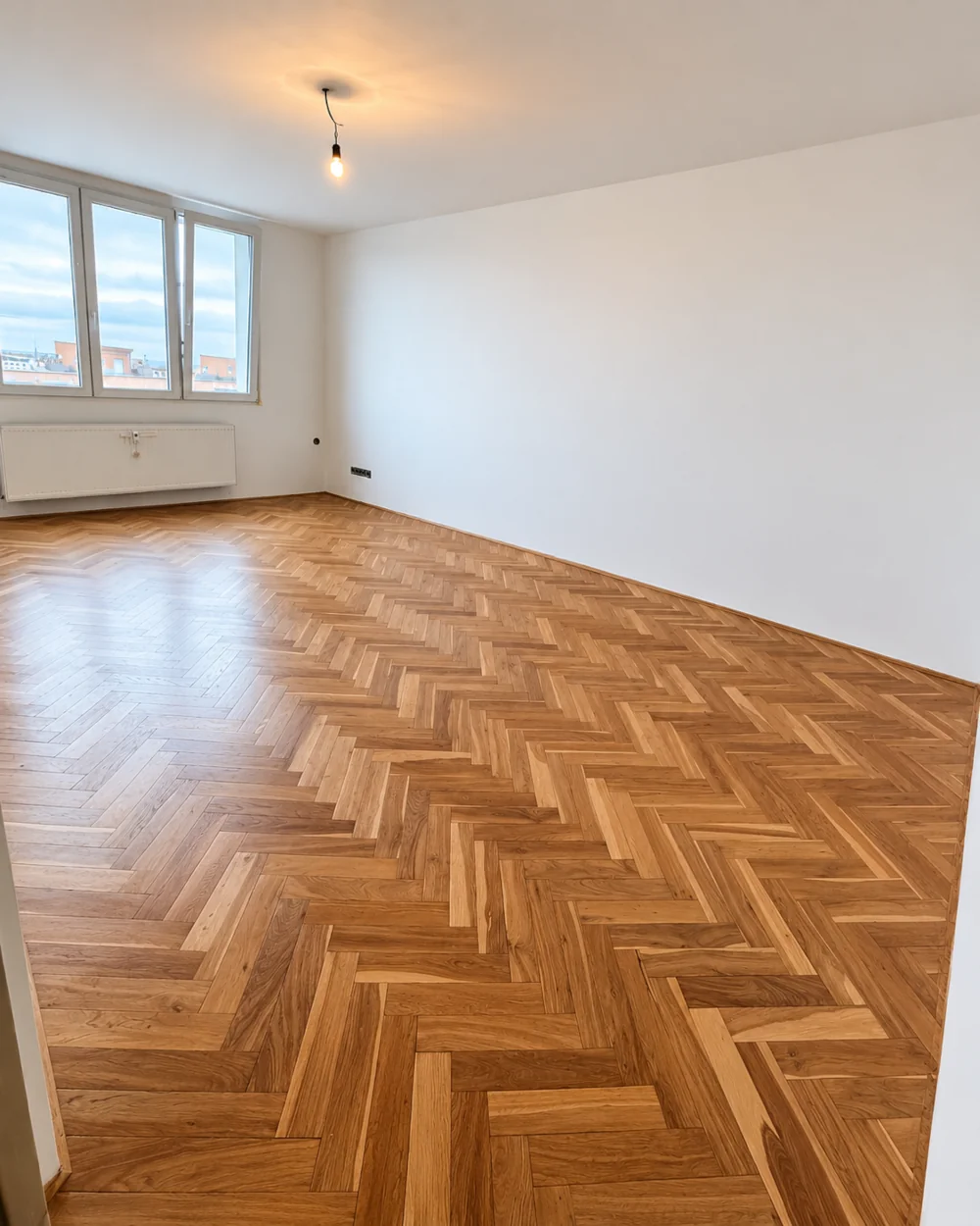Renovovaná dřevěná parketová podlaha se vzorem rybí kosti a obnovenou povrchovou úpravou.