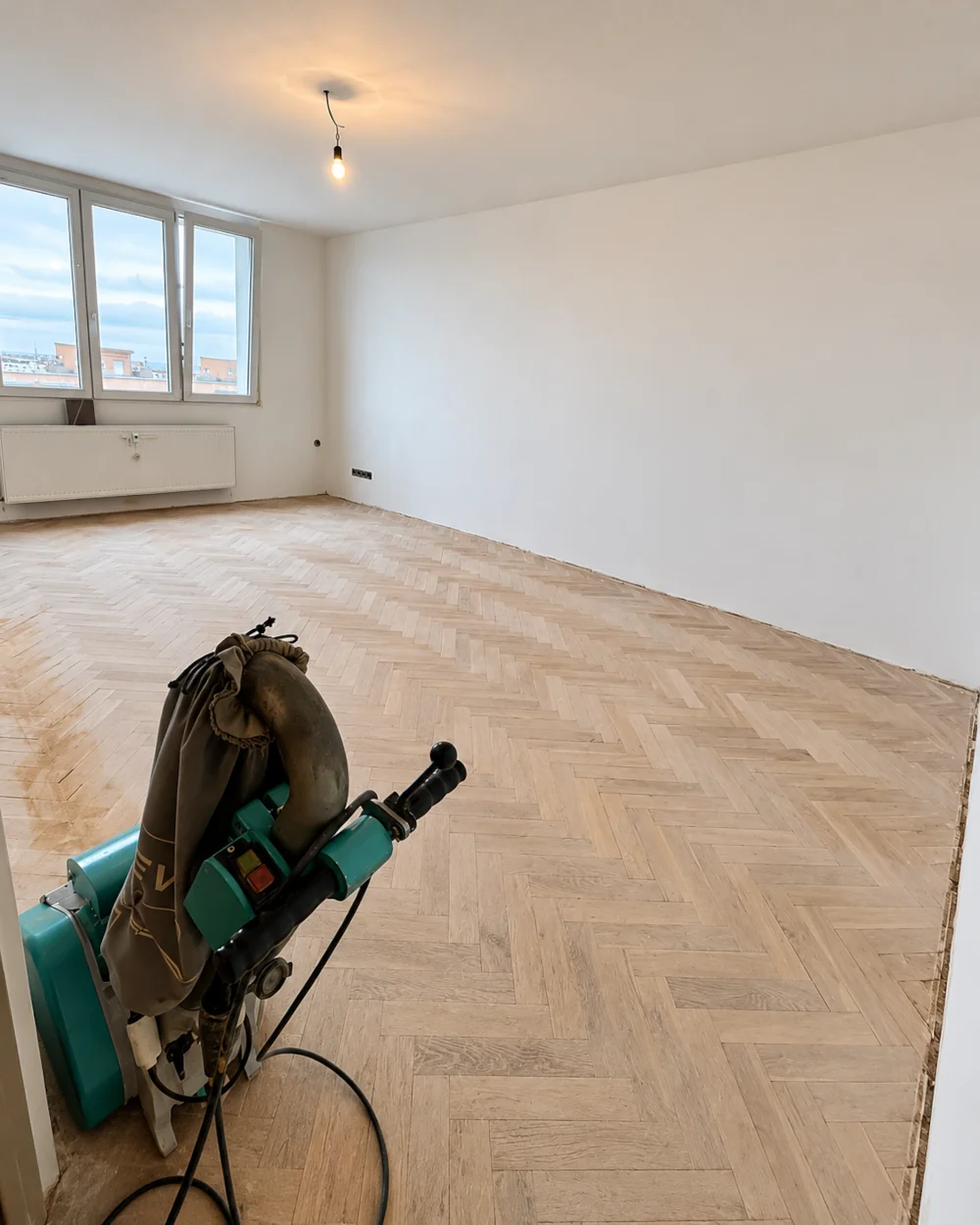 Opotřebená parketová podlaha se zašedlým povrchem, skvrnami a stopami používání před renovací.